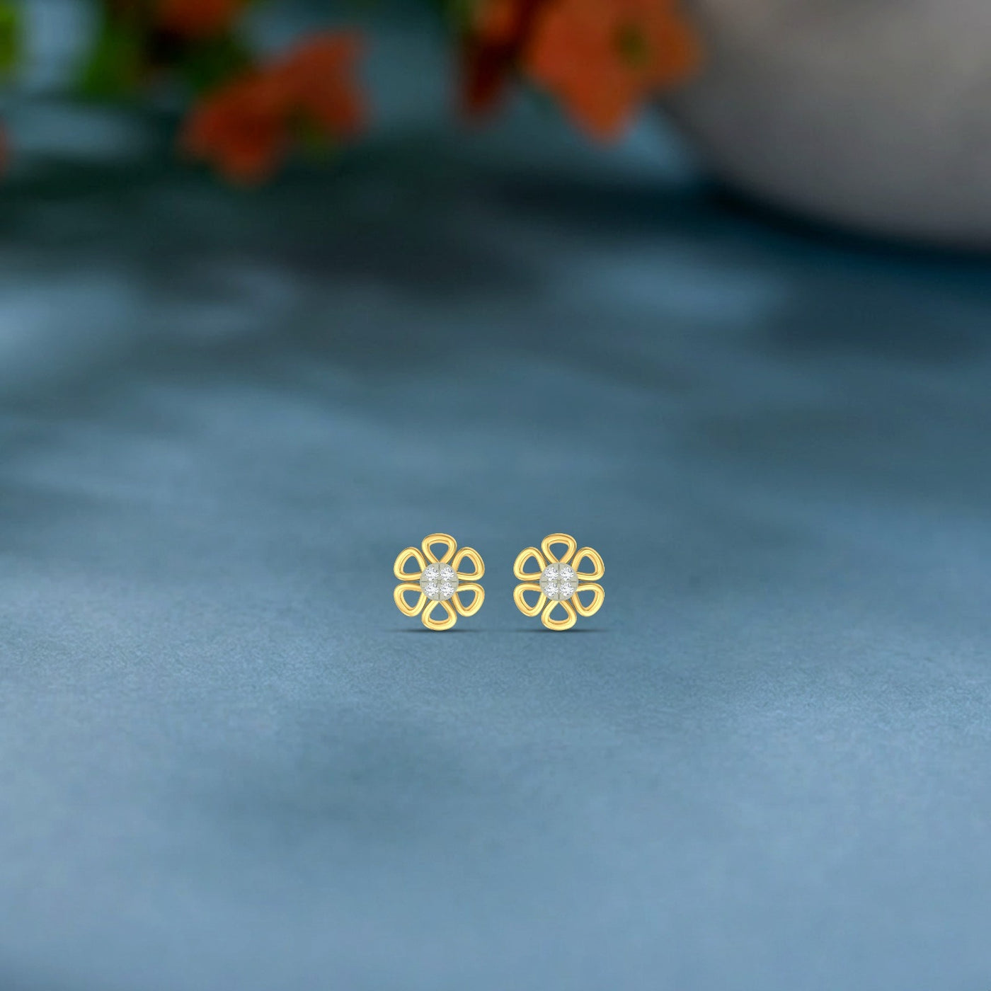 Gold and dimaond floral stud earrings on a blue fabric background.
