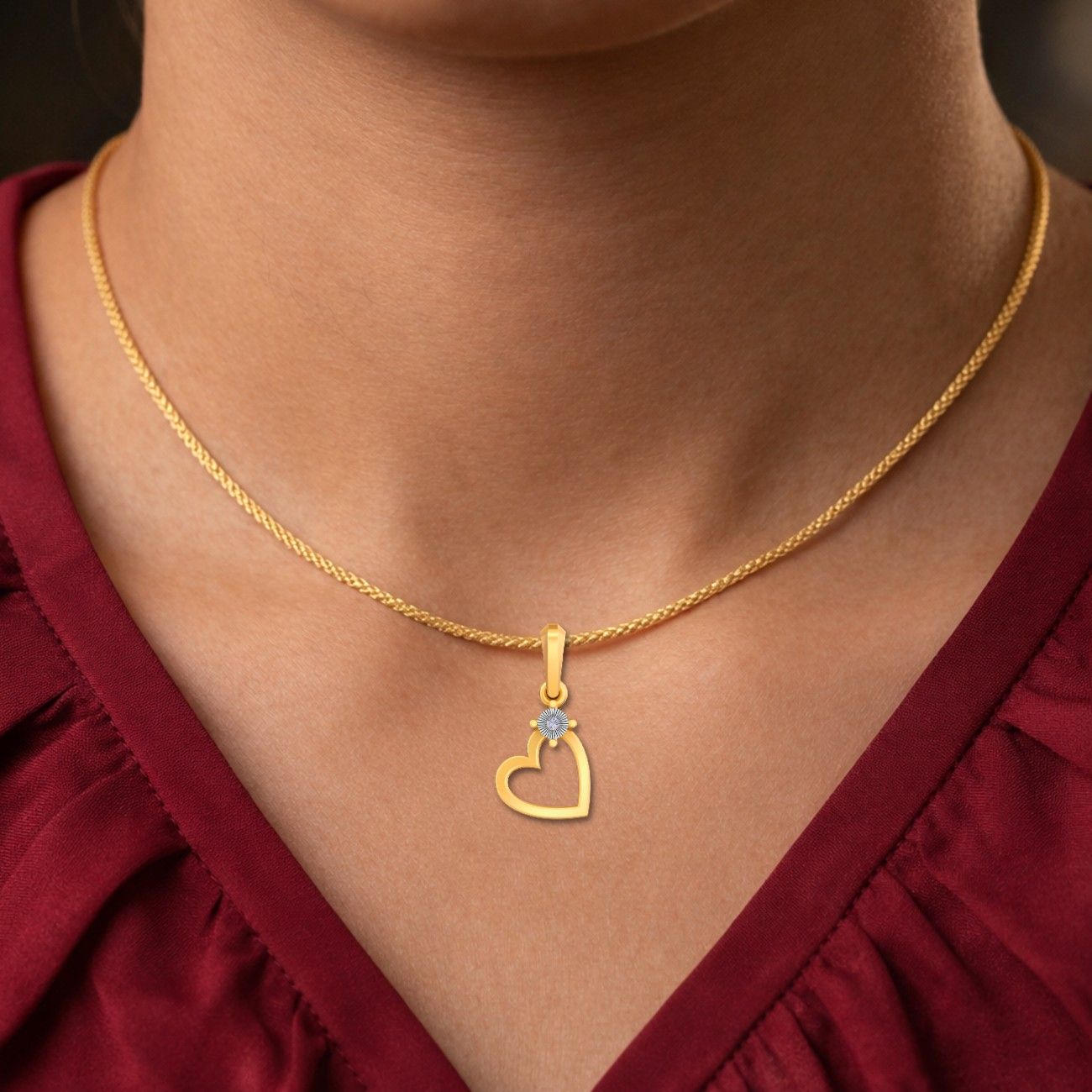 Gold necklace with a heart-shaped pendant worn by a person in a red garment.