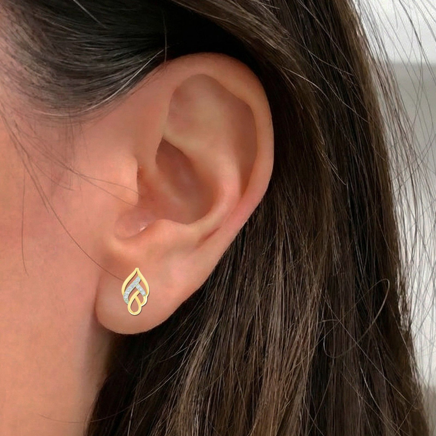 Close-up of an ear wearing a gold and diamond leaf-design earring.