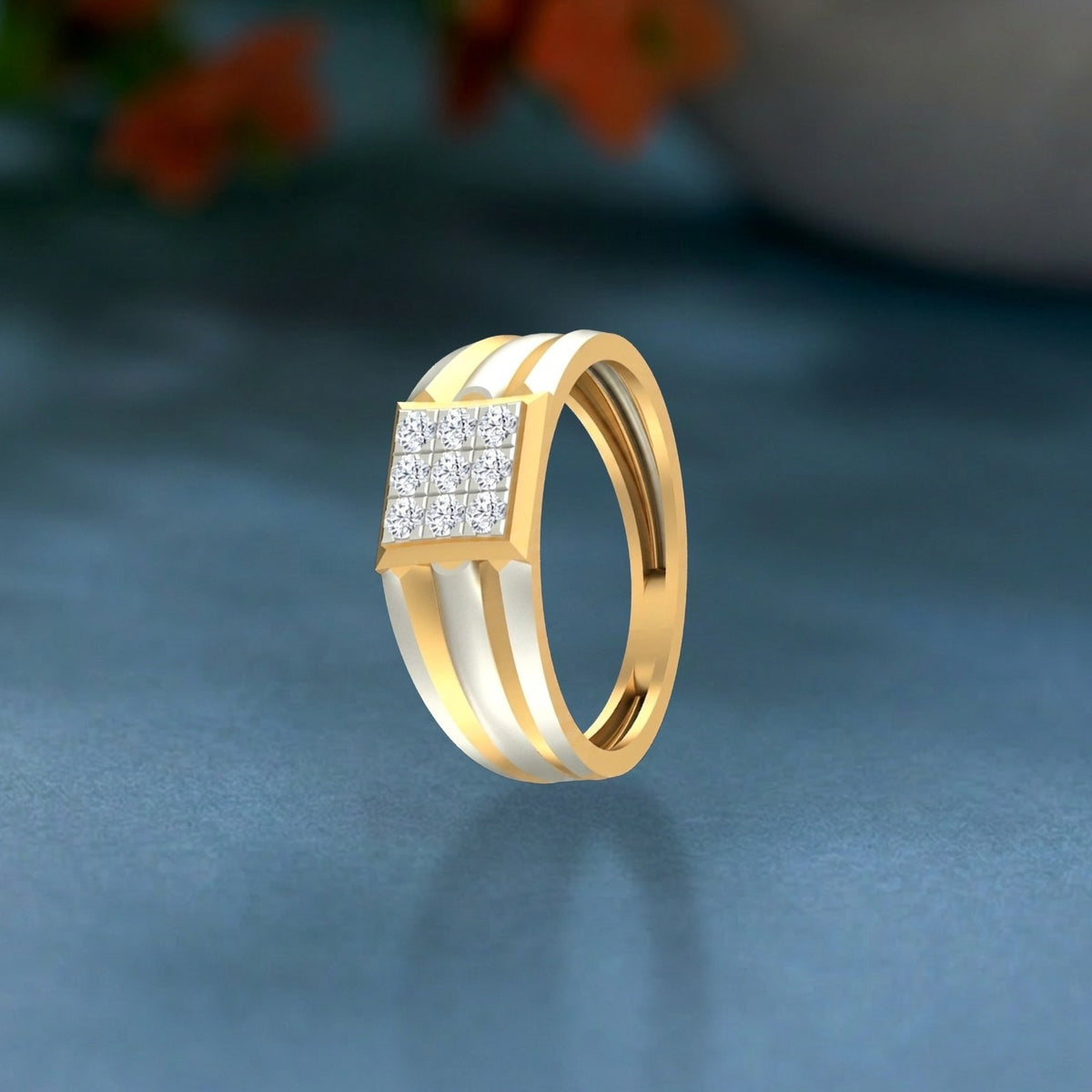 Gold and diamond ring featuring a square diamond cluster on the top, set against a teal surface.