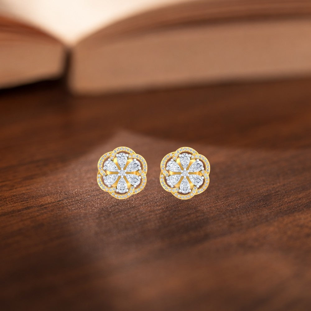 A pair of yellow gold earrings with diamond accents, featuring a floral design on a wooden surface.