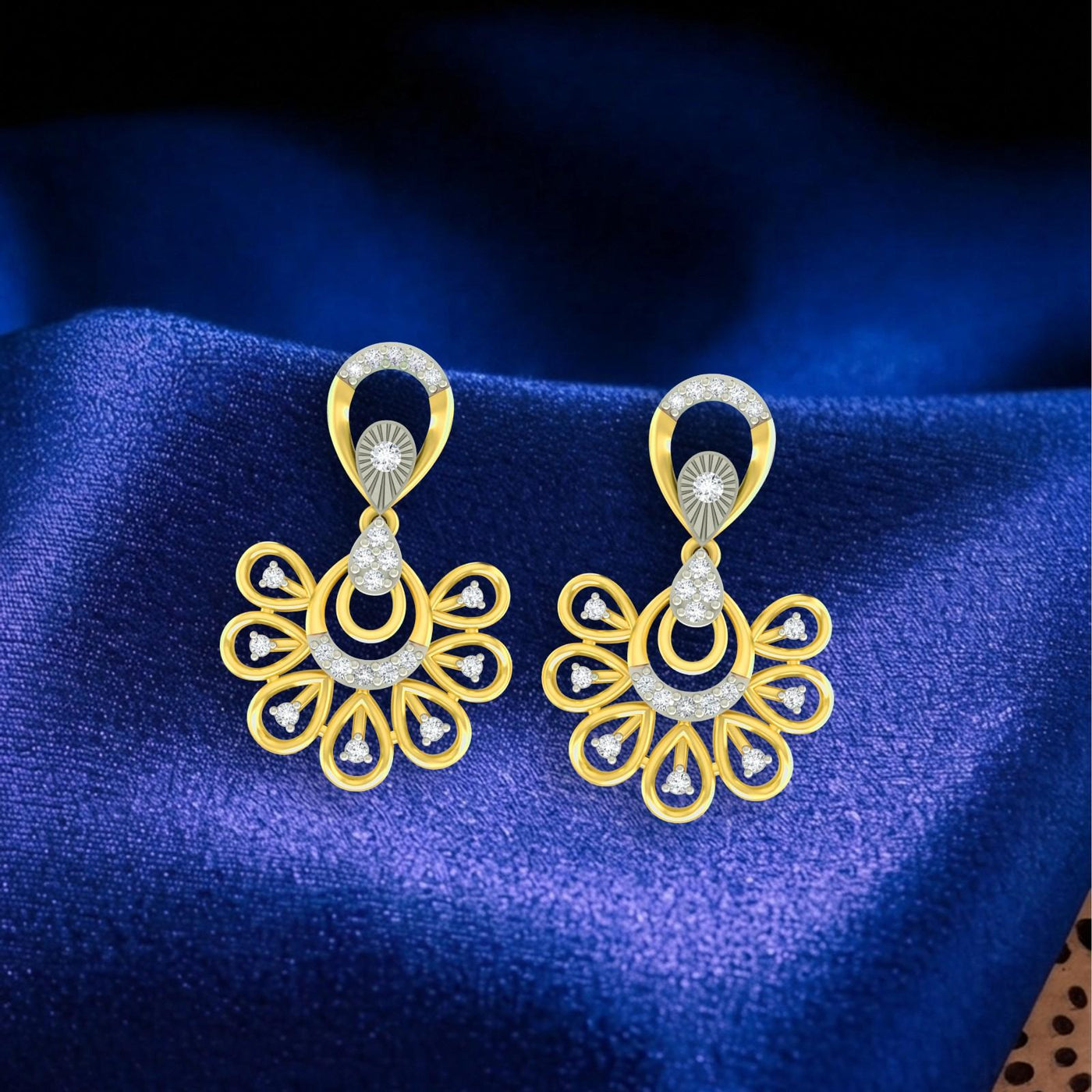 A pair of gold-toned dangler earrings with intricate floral and circular design on a blue fabric background.