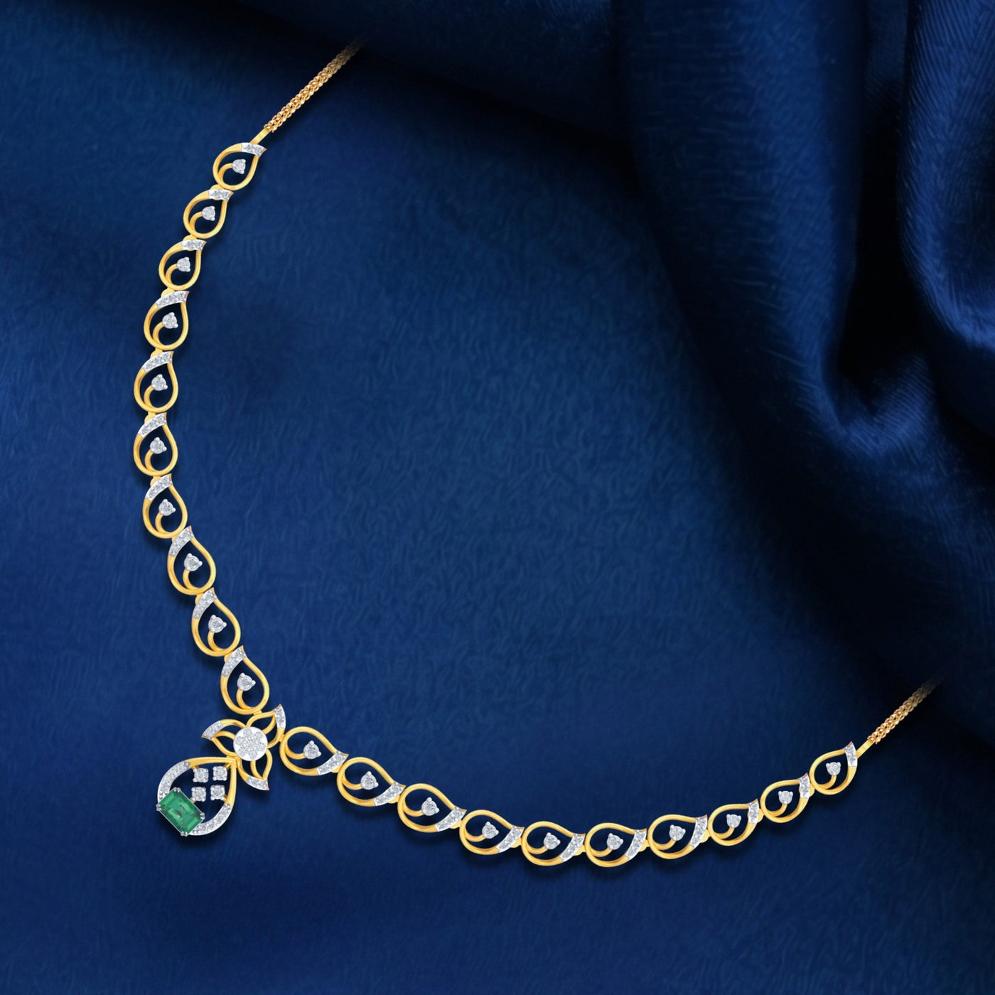 Gold and diamond necklace with green gemstone on a blue fabric background