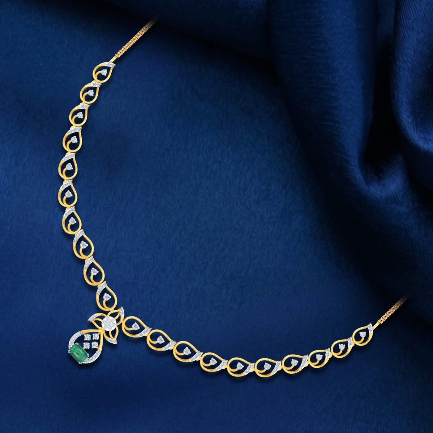 A gold and diamond necklace with a green gemstone, displayed on dark blue satin fabric.