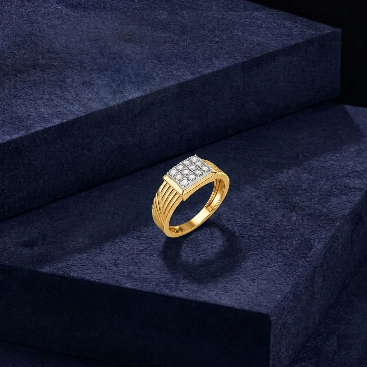 A gold ring with a square diamond cluster setting, displayed on a dark navy blue velvet block.
