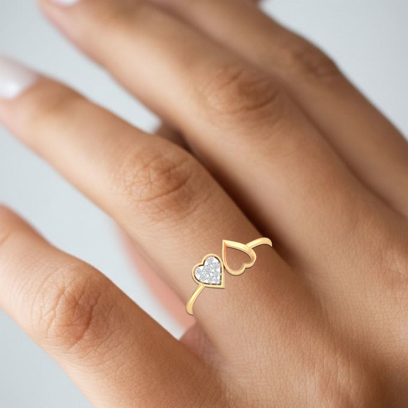 Gold ring with a heart design on a person's finger against a neutral background