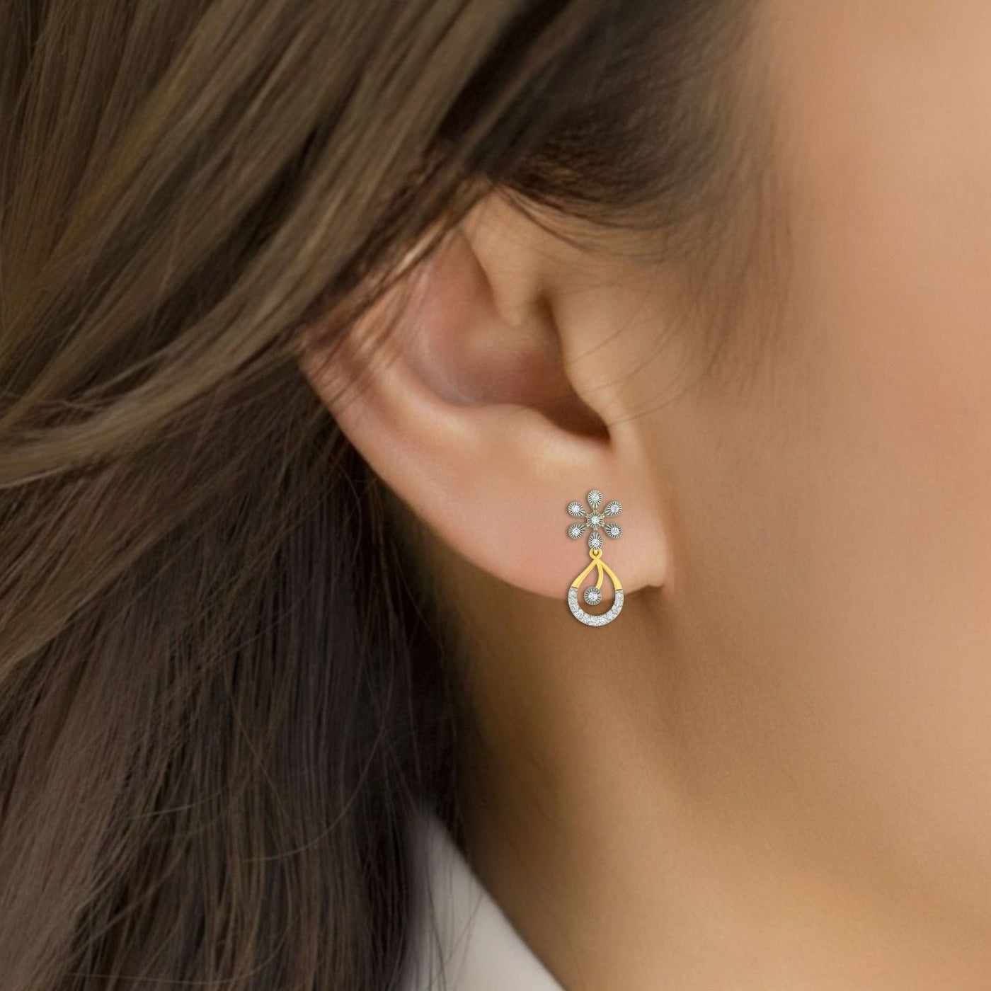 Close-up of an ear wearring a pair of yellow gold and diamond floral drop earrings.