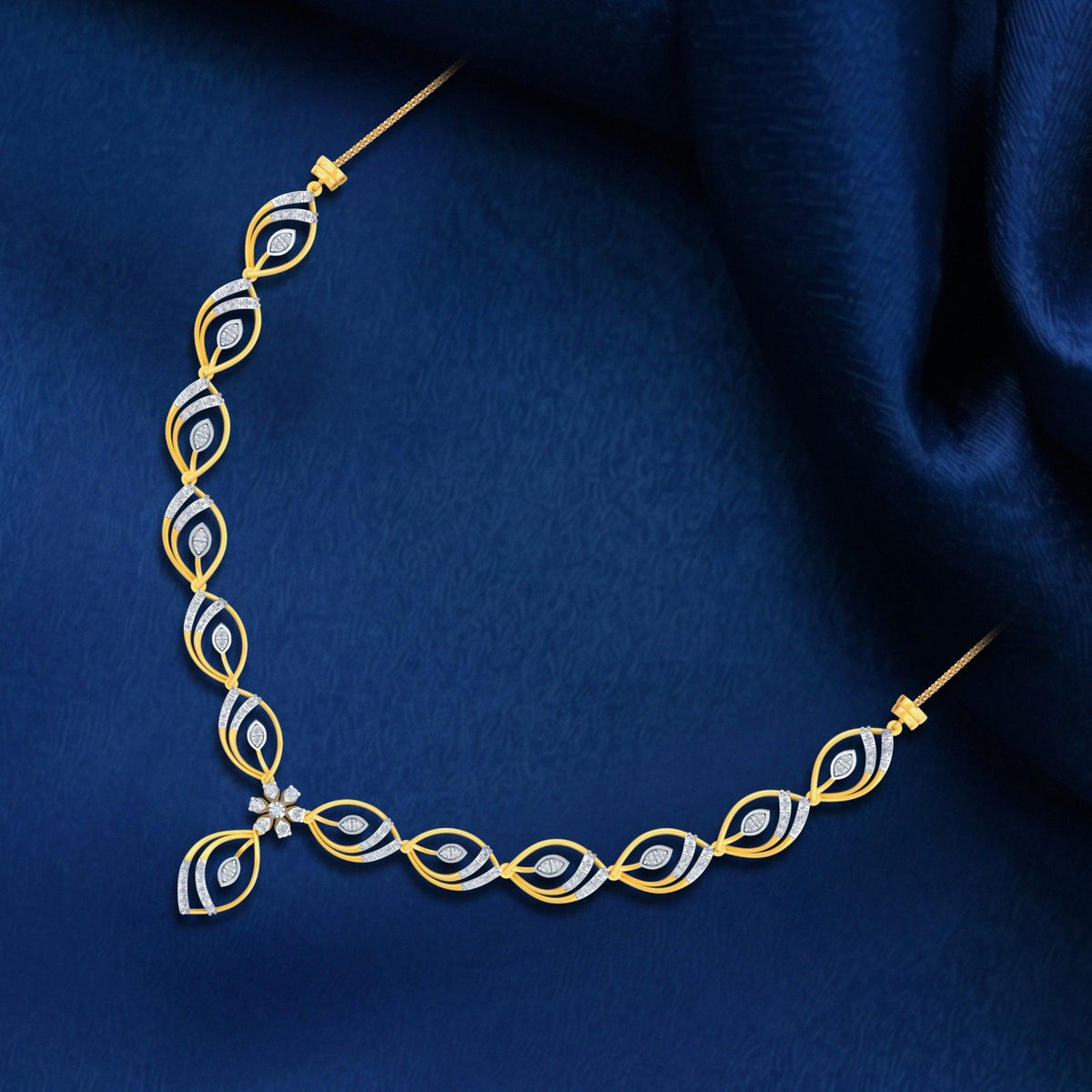 A gold and diamond necklace with a central floral motif, displayed on a textured dark blue fabric background.