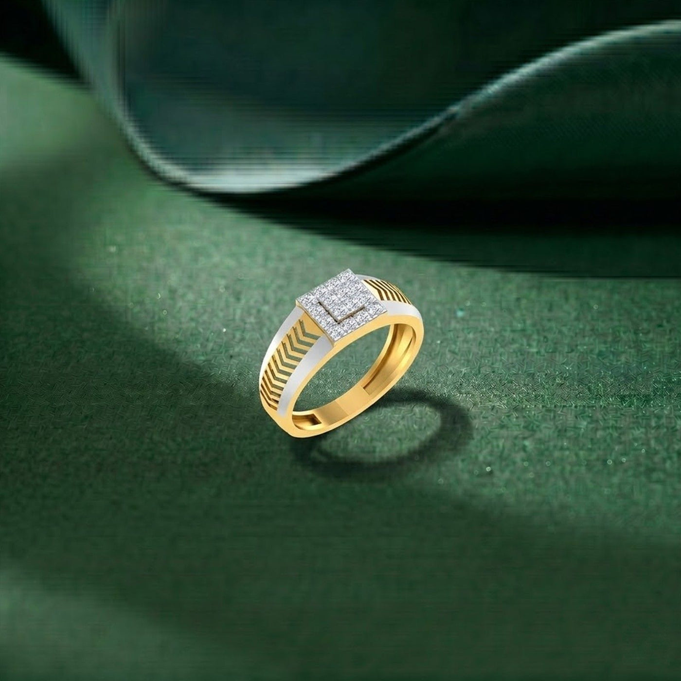 A gold ring with a square diamond set top and textured, resting on a dark green textured surface with a blurred green background.