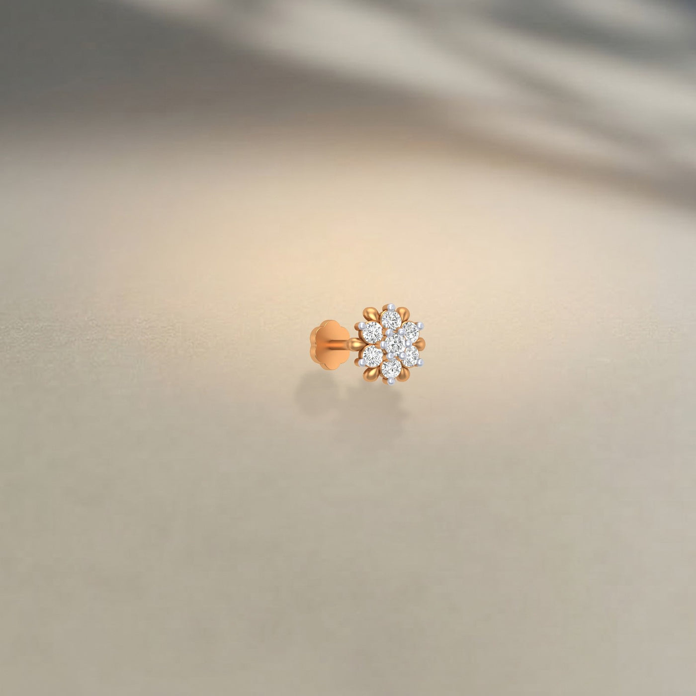 Yellow gold and diamond stud nose pin with small diamonds on a beige background