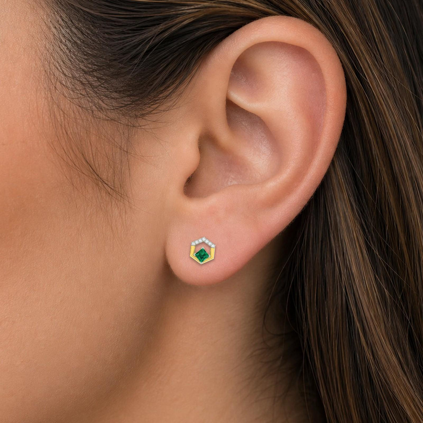 Close-up shot of a geometric, two-tone yellow gold open-hexagon earrings featuring central square green gemstones earring.