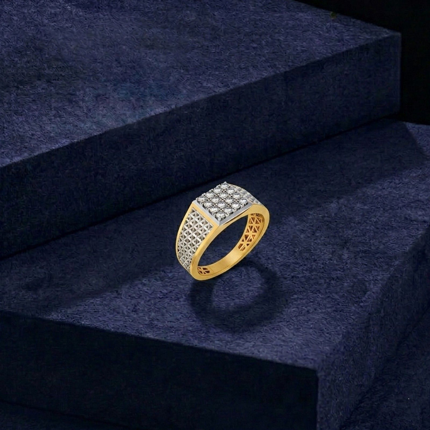 A gold ring with a square face paved with a textured gold pattern on the other, displayed on a dark navy velvet block.