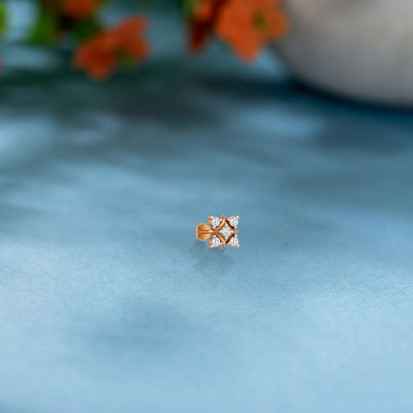 yellow gold and diamond stud nose pin on a light blue fabric background