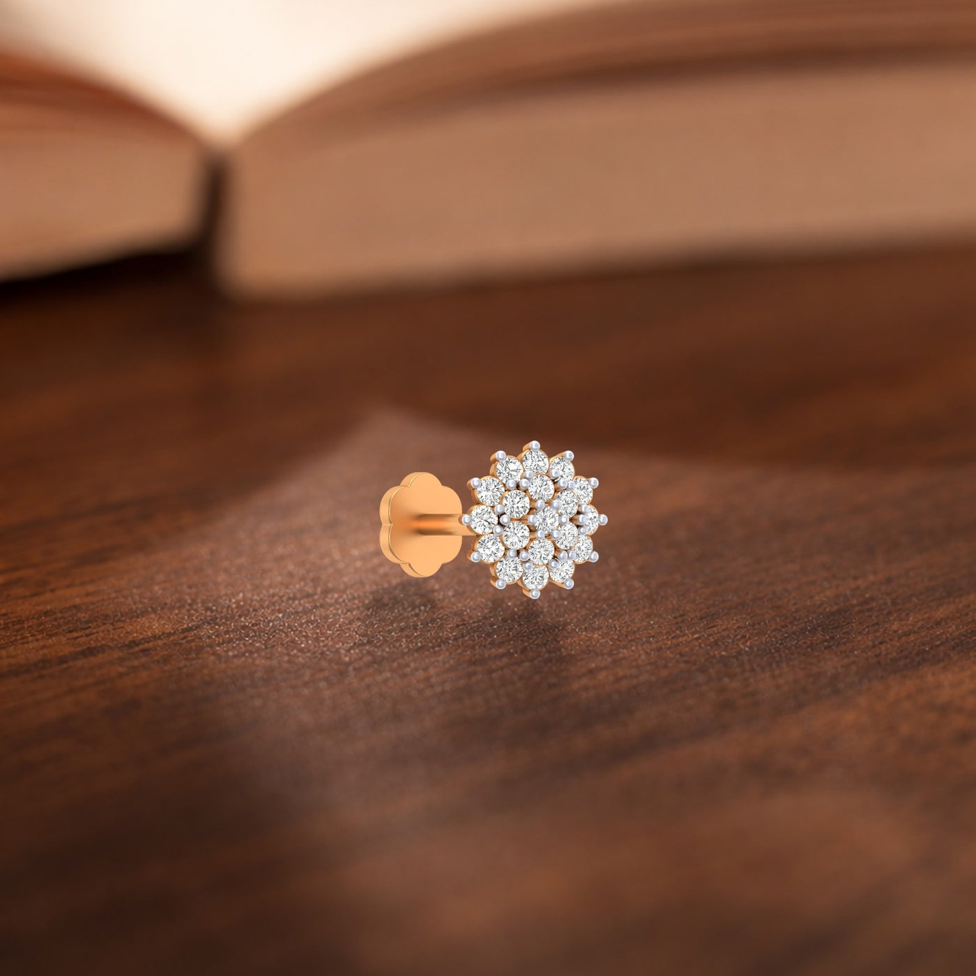 Pair of yellow gold and diamond stud nose pin on a wooden surface with a blurred book in the background.