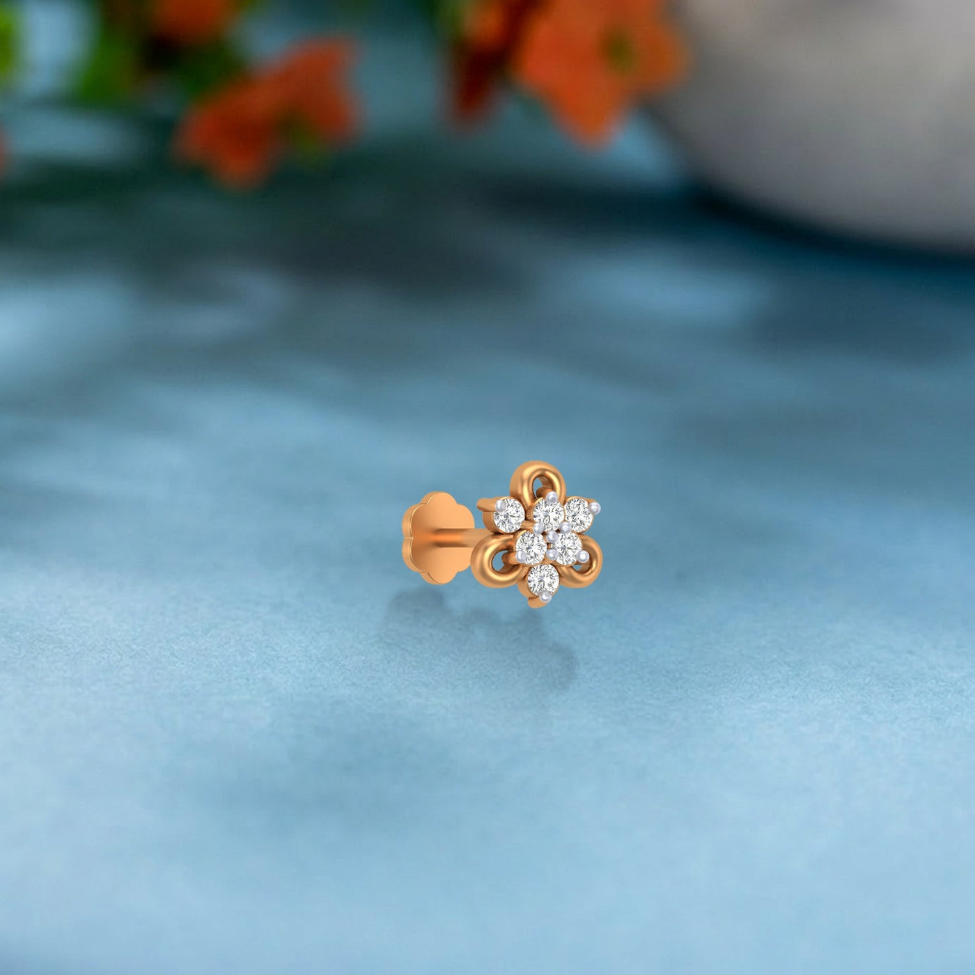 yellow gold and diamond stud nose pin with floral design on a light blue fabric background