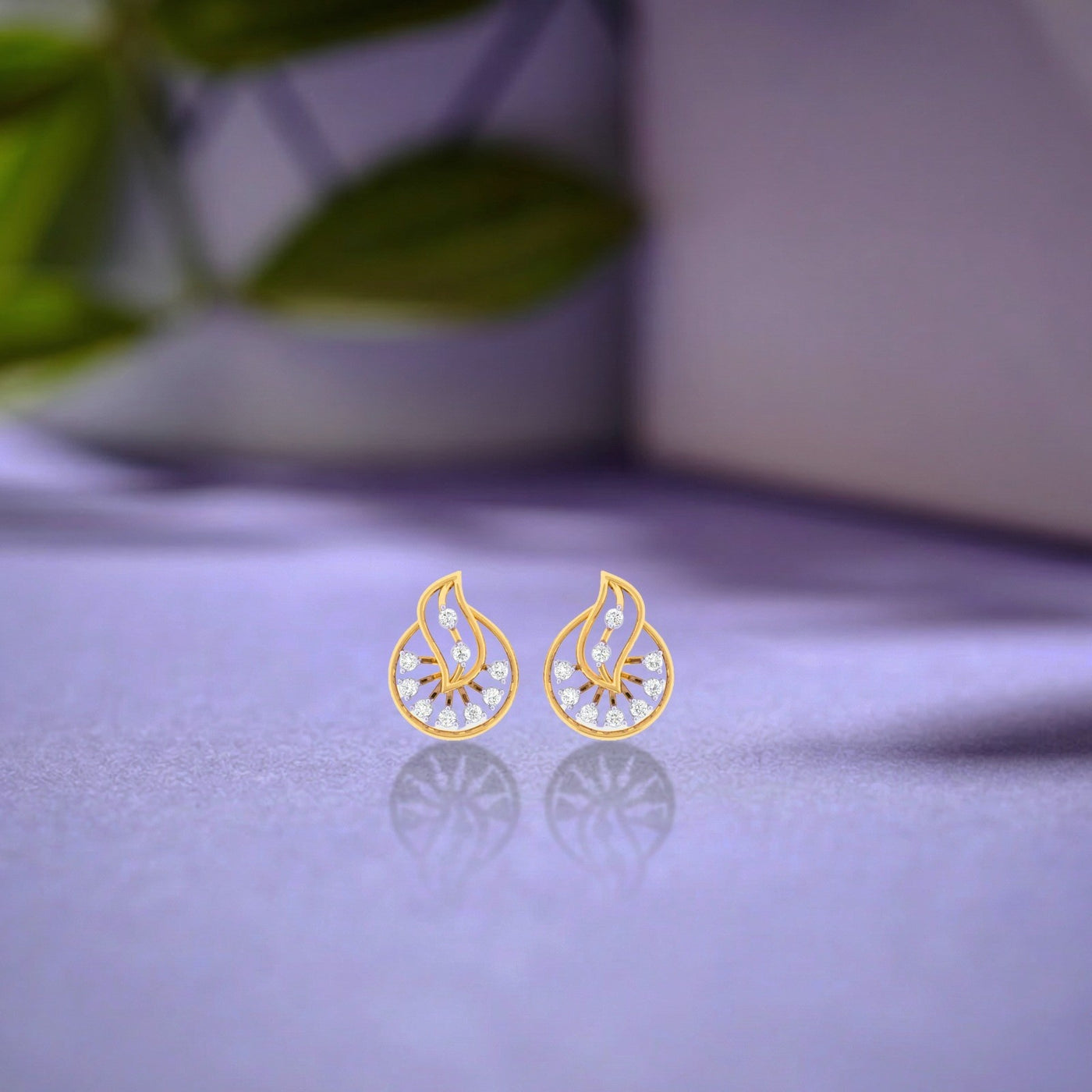 Pair of gold and diamond round shaped stud earrings with leaf-design on a refective surface.