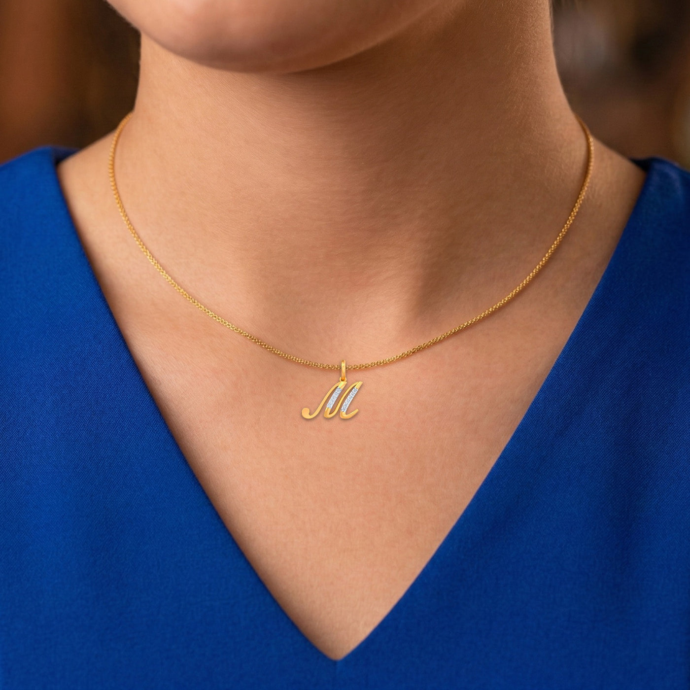 Gold necklace with a 'M' pendant worn by a person in a blue top.