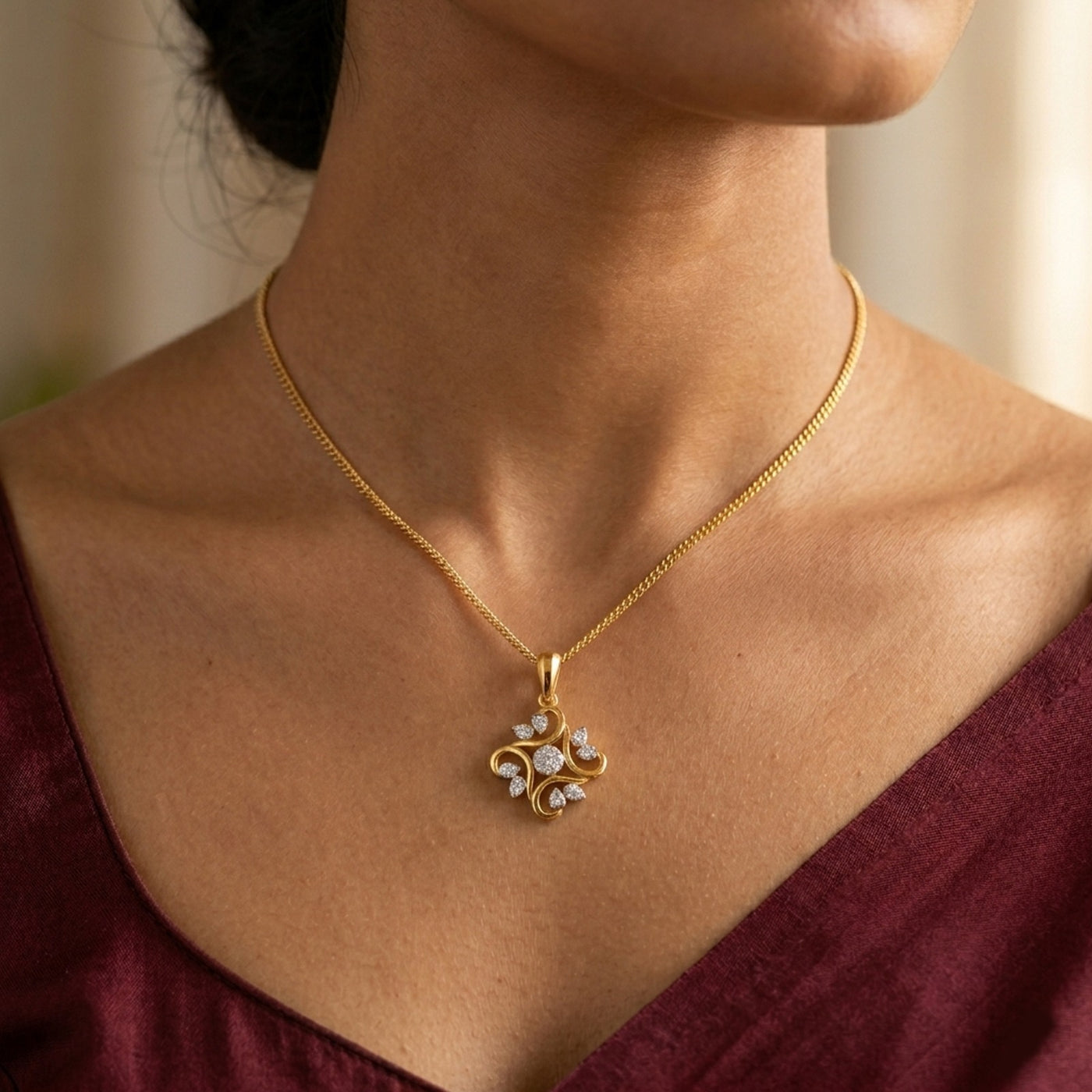Gold necklace with a floral pendant worn by a person in a burgundy top.