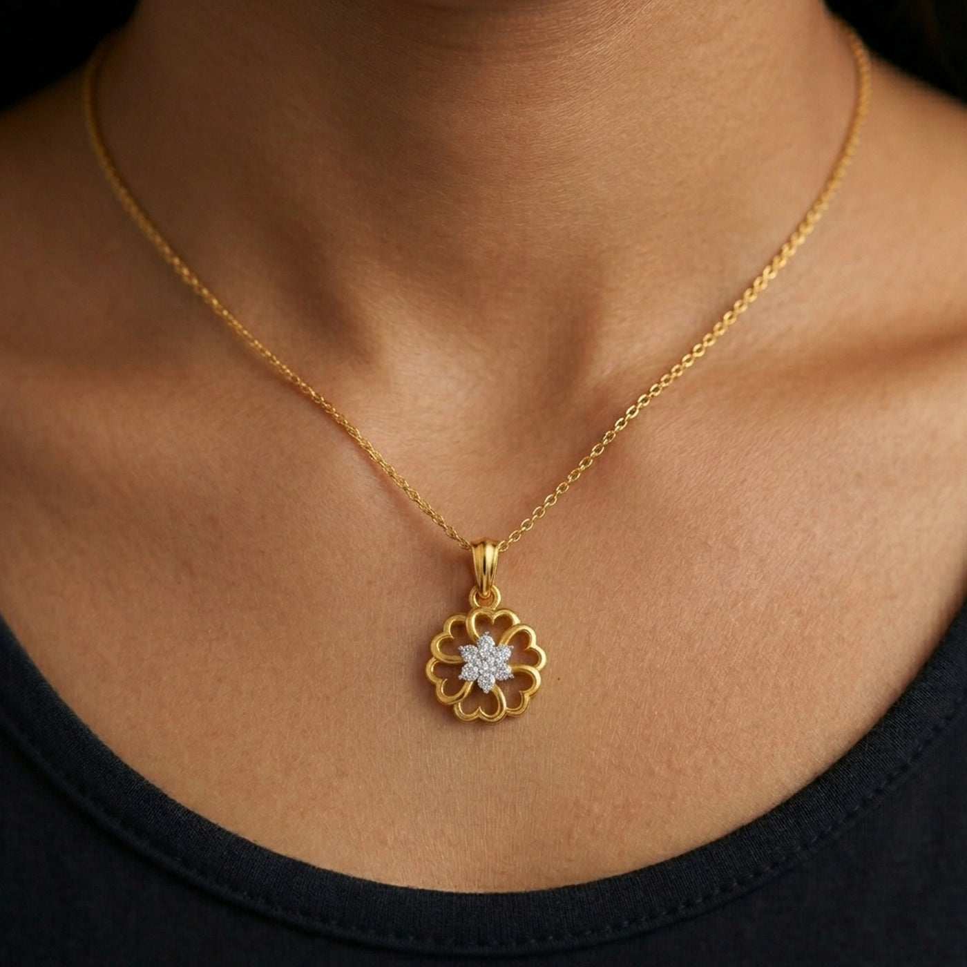 Gold necklace with a floral pendant on a person wearing a black top.