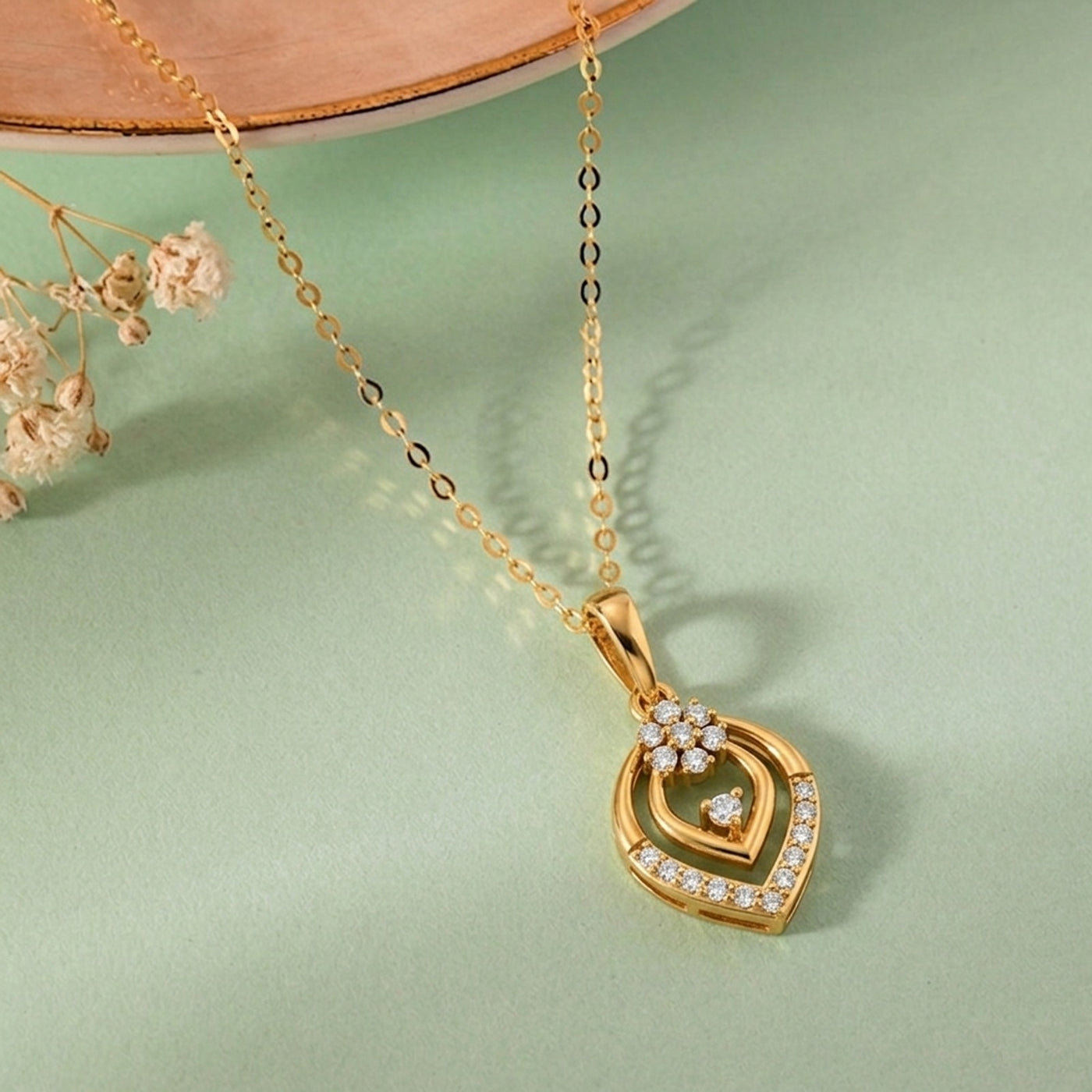 Gold necklace with a heart-shaped pendant on a light green background