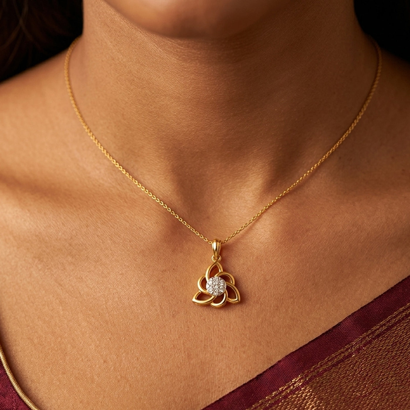 Gold necklace with a diamond pendant on a person wearing a maroon saree.