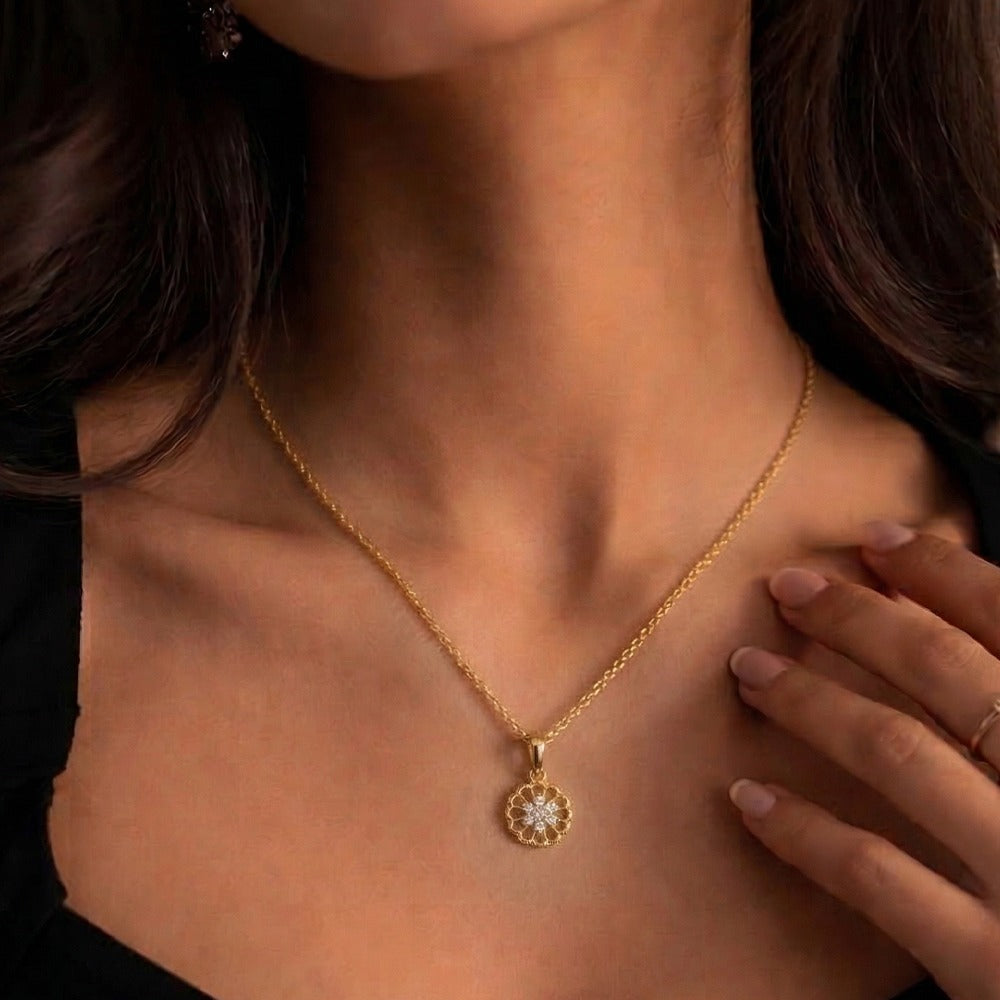 Gold with a pendant worn by a person, with a hand touching the chest.