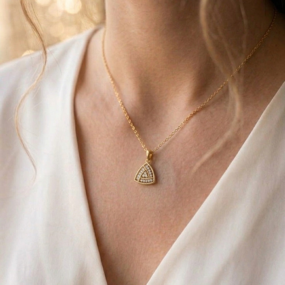 Gold with a triangular pendant worn by a person in a white outfit.