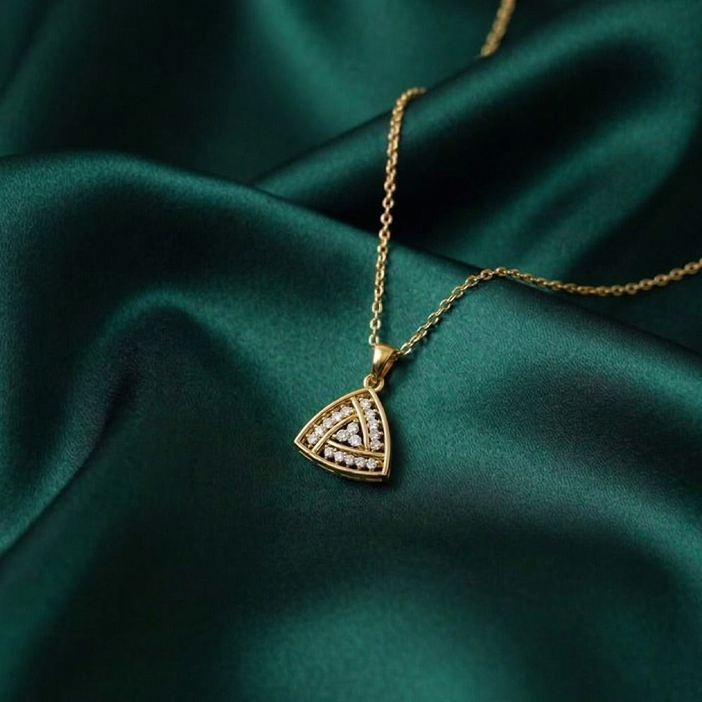 Gold triangular pendant on a green fabric background