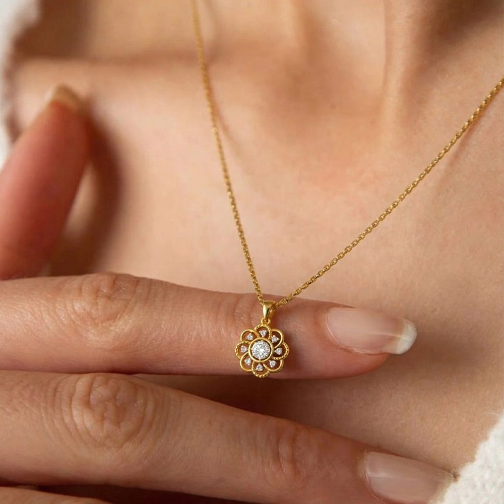 Gold and diamond floral pendant held by a hand against a soft background