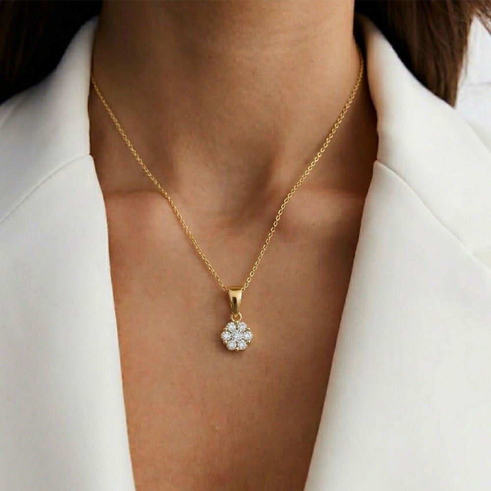 Gold necklace with a diamond pendant worn by a person in a white outfit.