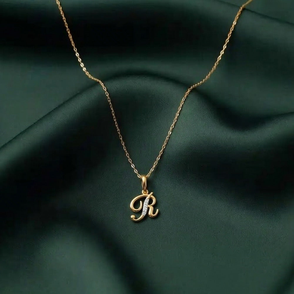 Gold necklace with a 'R' pendant on a dark green fabric background