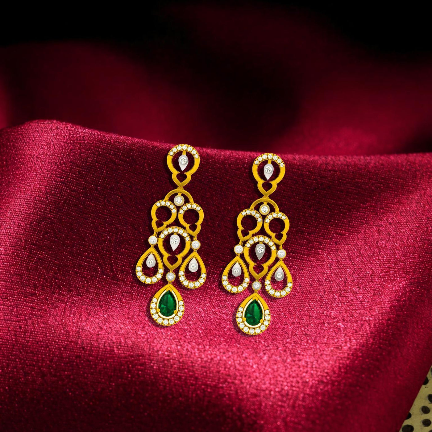 Gold and diamond teardrop-shaped earrings with clear gemstones on a red fabric background.