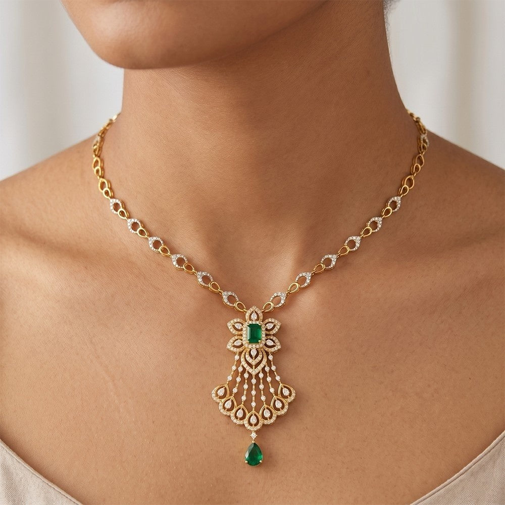 Gold and diamond necklace with green gemstone on a person against a neutral background.