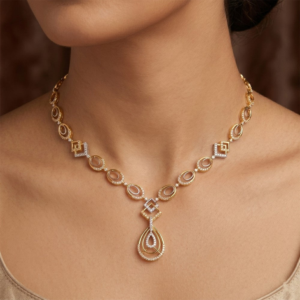 Gold necklace with a teardrop design on a person's neck against a blurred background.