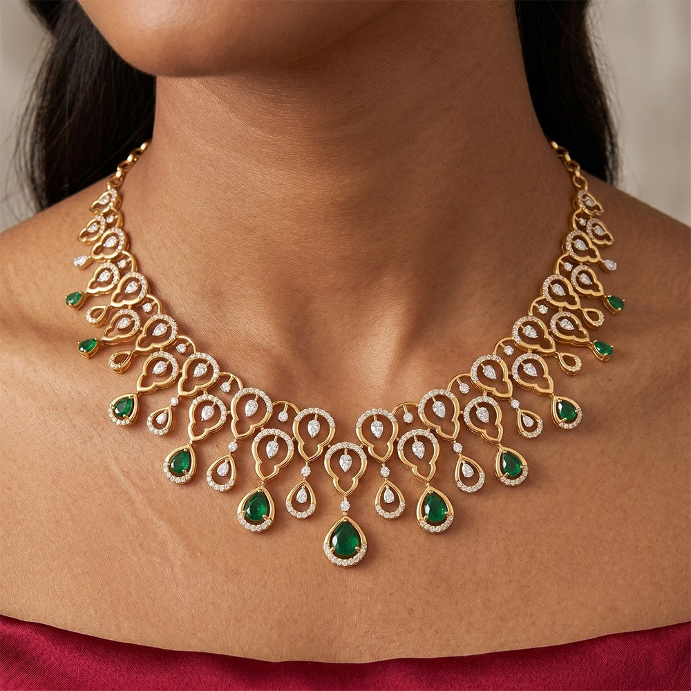 A gold-toned statement necklace with emerald-cut green gemstones and small clear stones, shown worn on a model's neck.