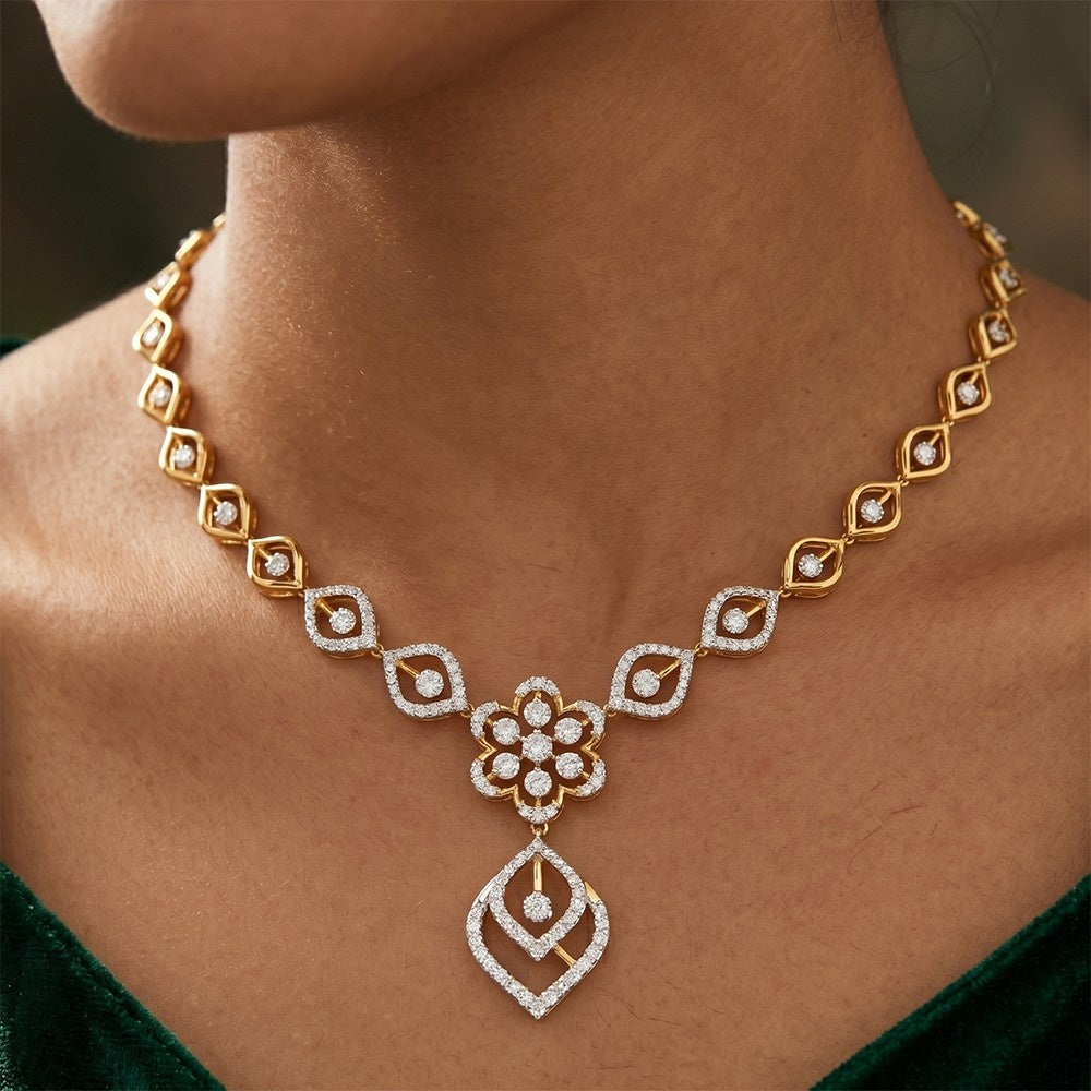 A close-up of a person wearing an elegant yellow gold and diamond necklace featuring a central floral design and a geometric drop pendant