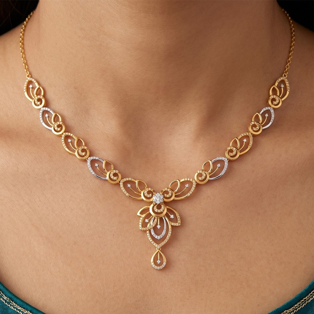 A close-up of a person wearing an elegant two-tone yellow and white gold necklace featuring diamond-accented swirl and leaf motifs.