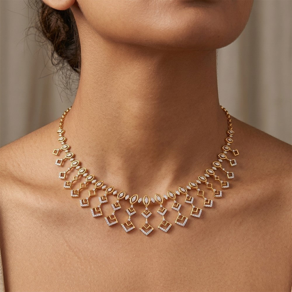 A close-up of a model wearing a gold geometric necklace, shown from the neck against a soft beige background.