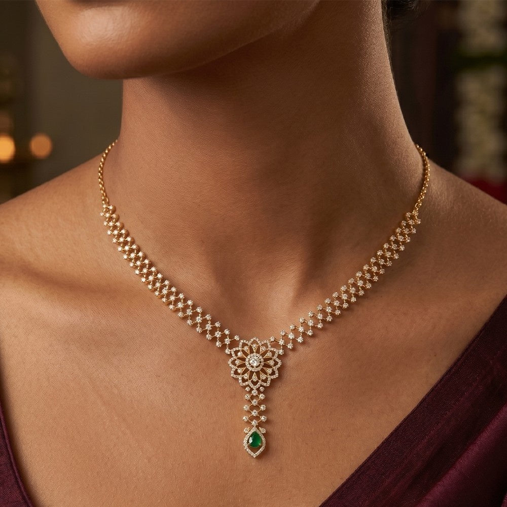 A close-up of a model wearing a gold and diamond necklace with a green teardrop gemstone.