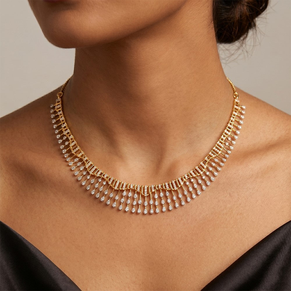 A gold-toned multi-strand necklace with dangling clear stones, worn on a model's neck against a neutral beige background.