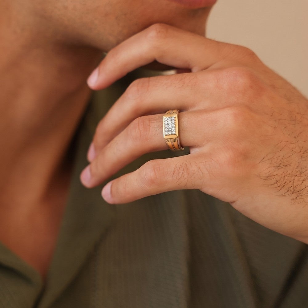 Close-up of a hand wearing a gold ring with a diamond pattern, against a neutral background.