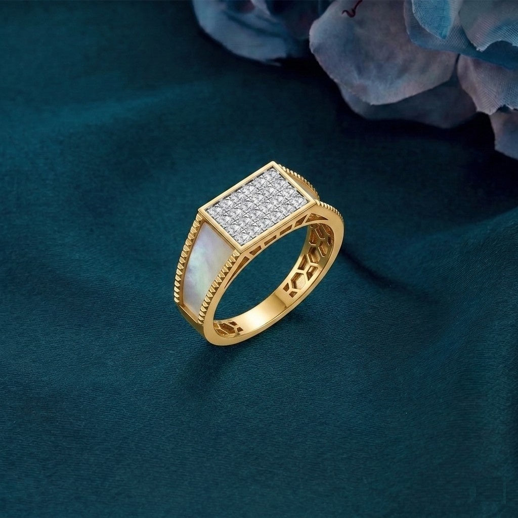 A gold signet-style ring with a rectangular pavé top, displayed on a dark teal fabric surface with blurred blue flowers in the background.