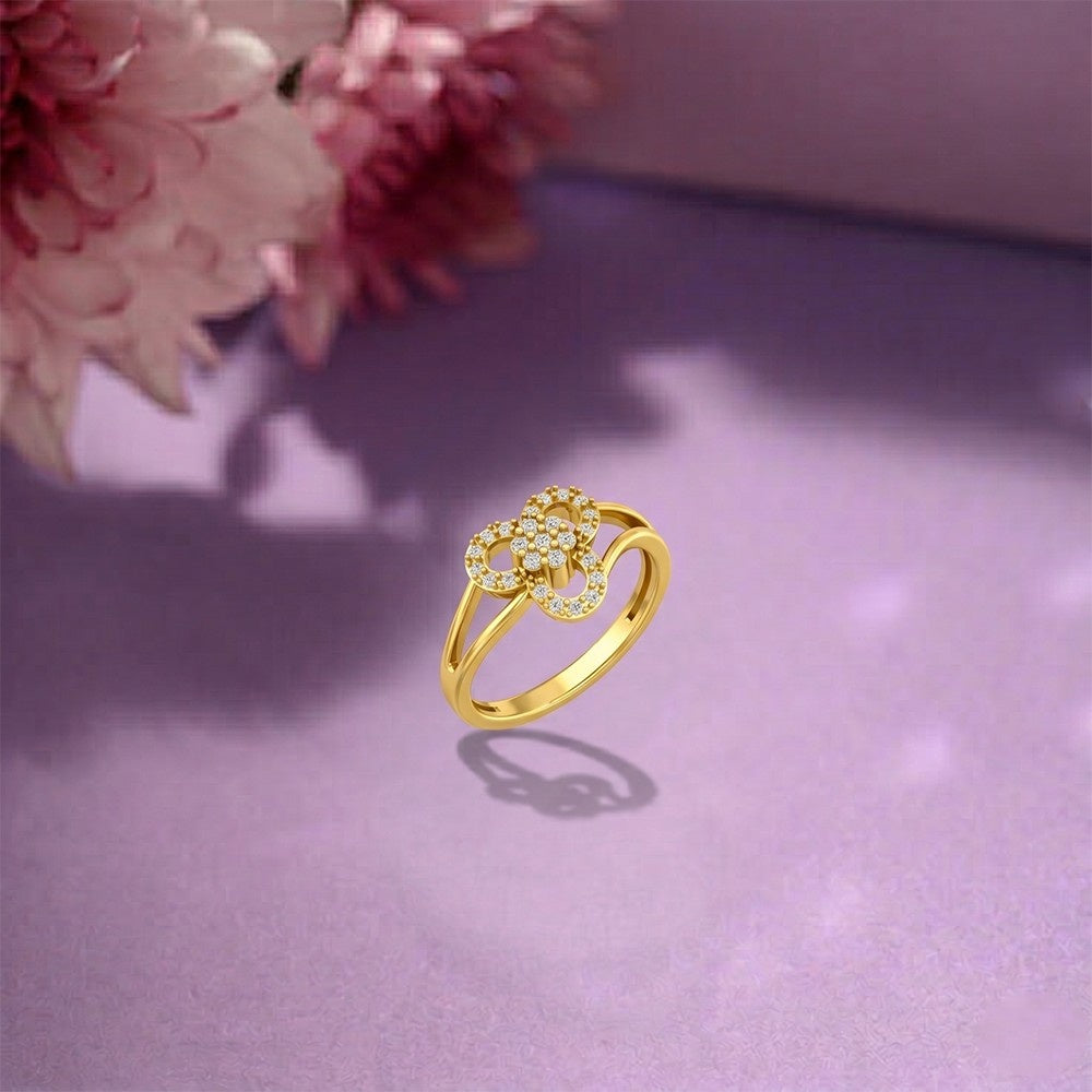 Gold ring with floral design on a purple surface with pink flowers in the background