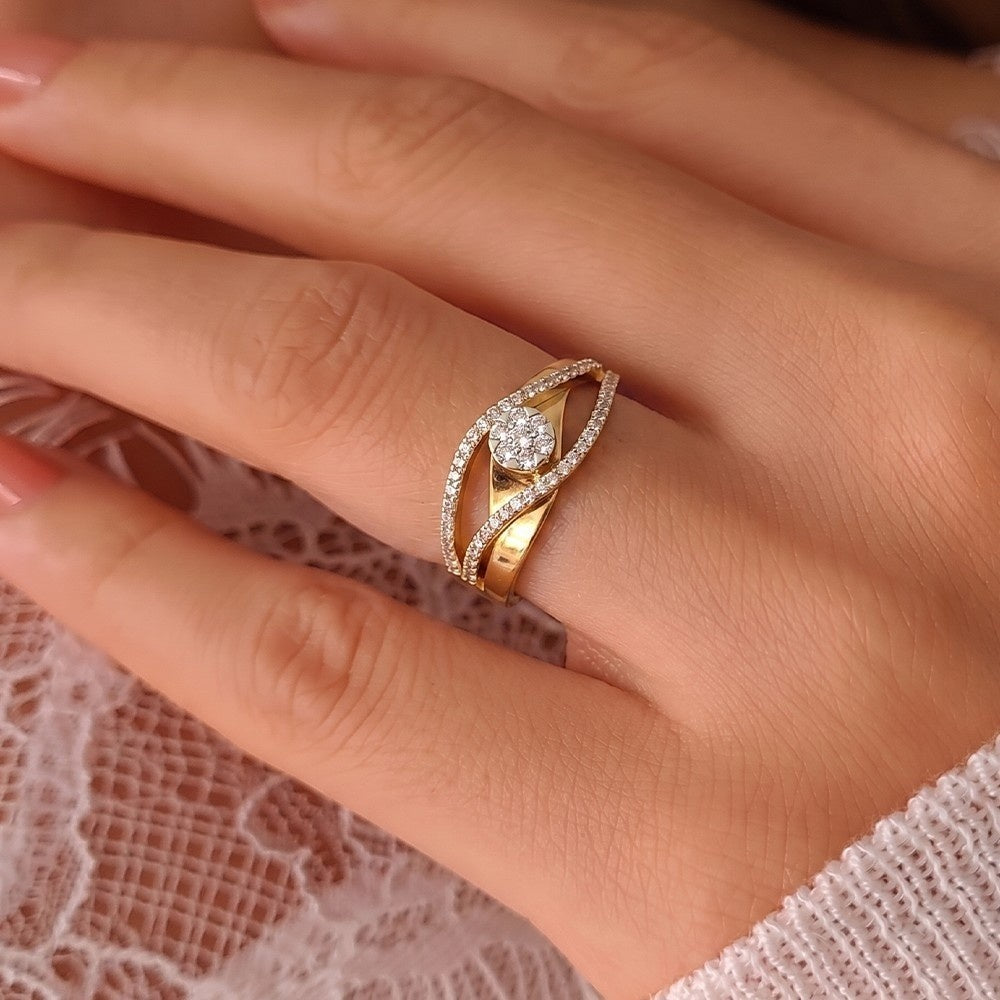 A gold and diamond  ring with a center round design, worn on a hand over a light pink lace fabric.