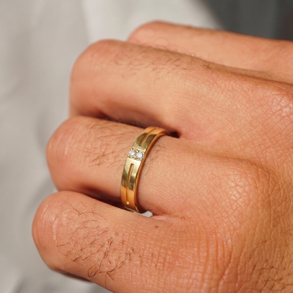 Gold ring with a diamond on a person's finger against a neutral background.