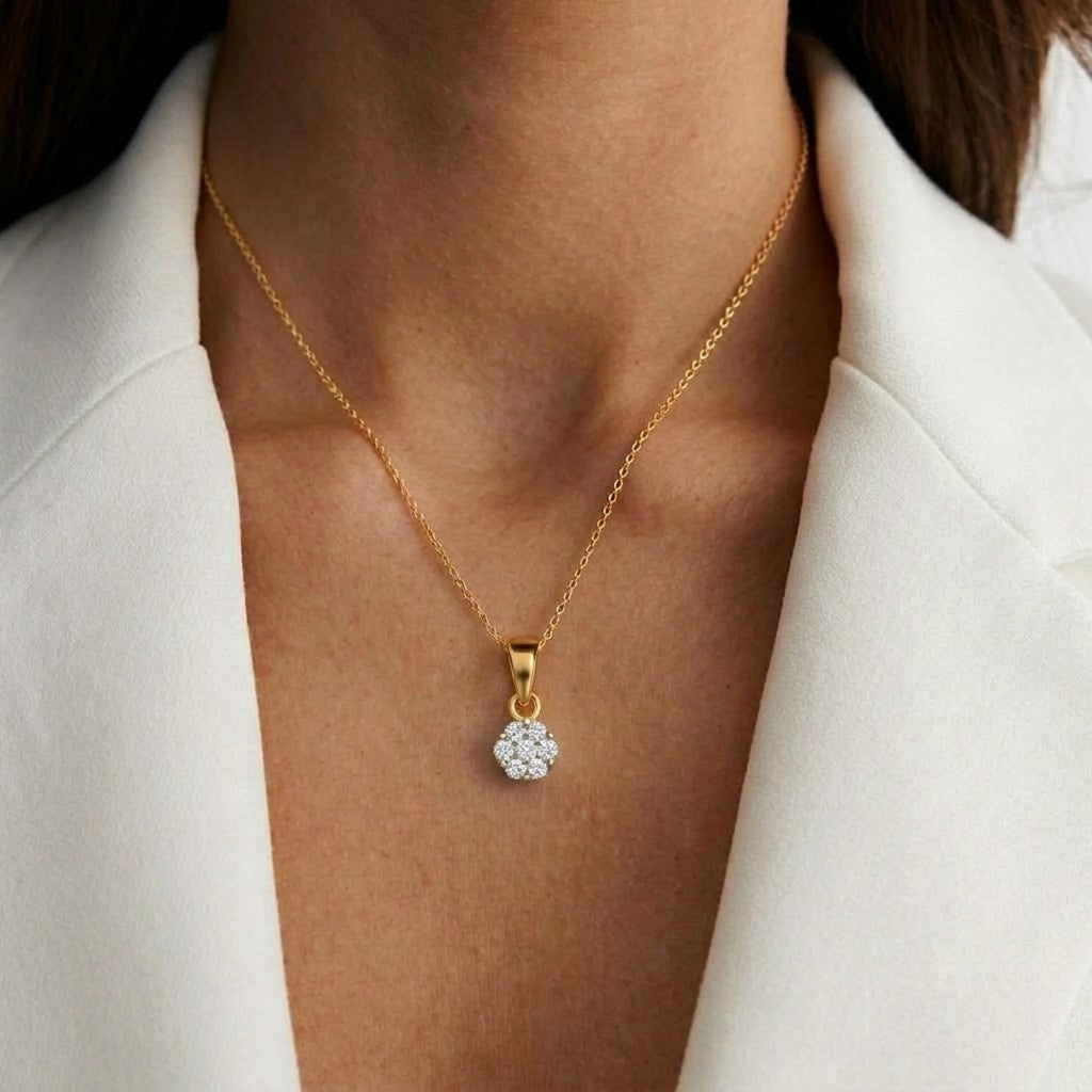 Gold necklace with a diamond pendant worn by a person in a white outfit.
